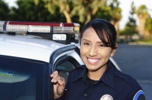 a smiling Hispanic police officer next to her patrol car.